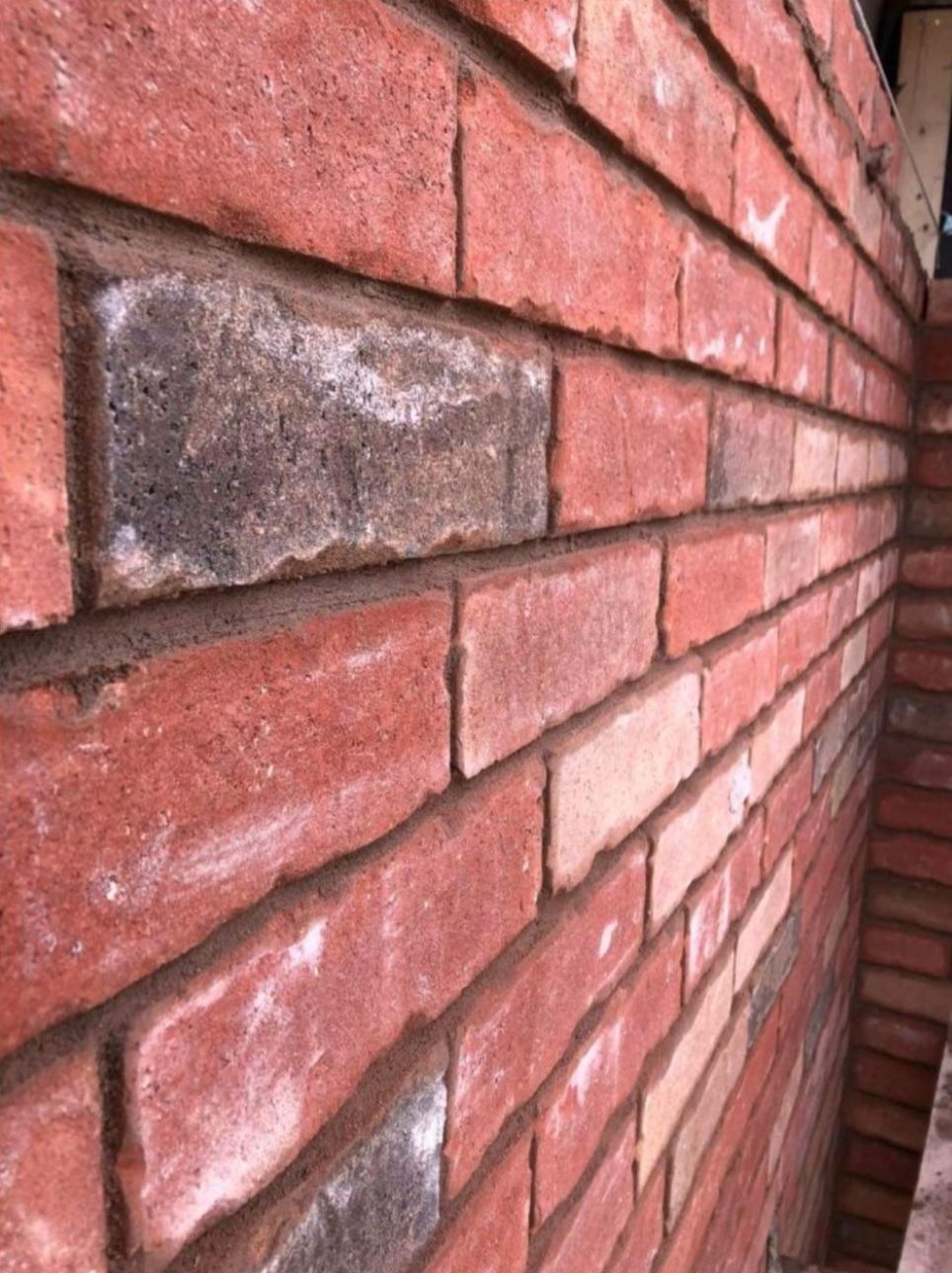 Close-up of a red brick wall with one replacement brick set in