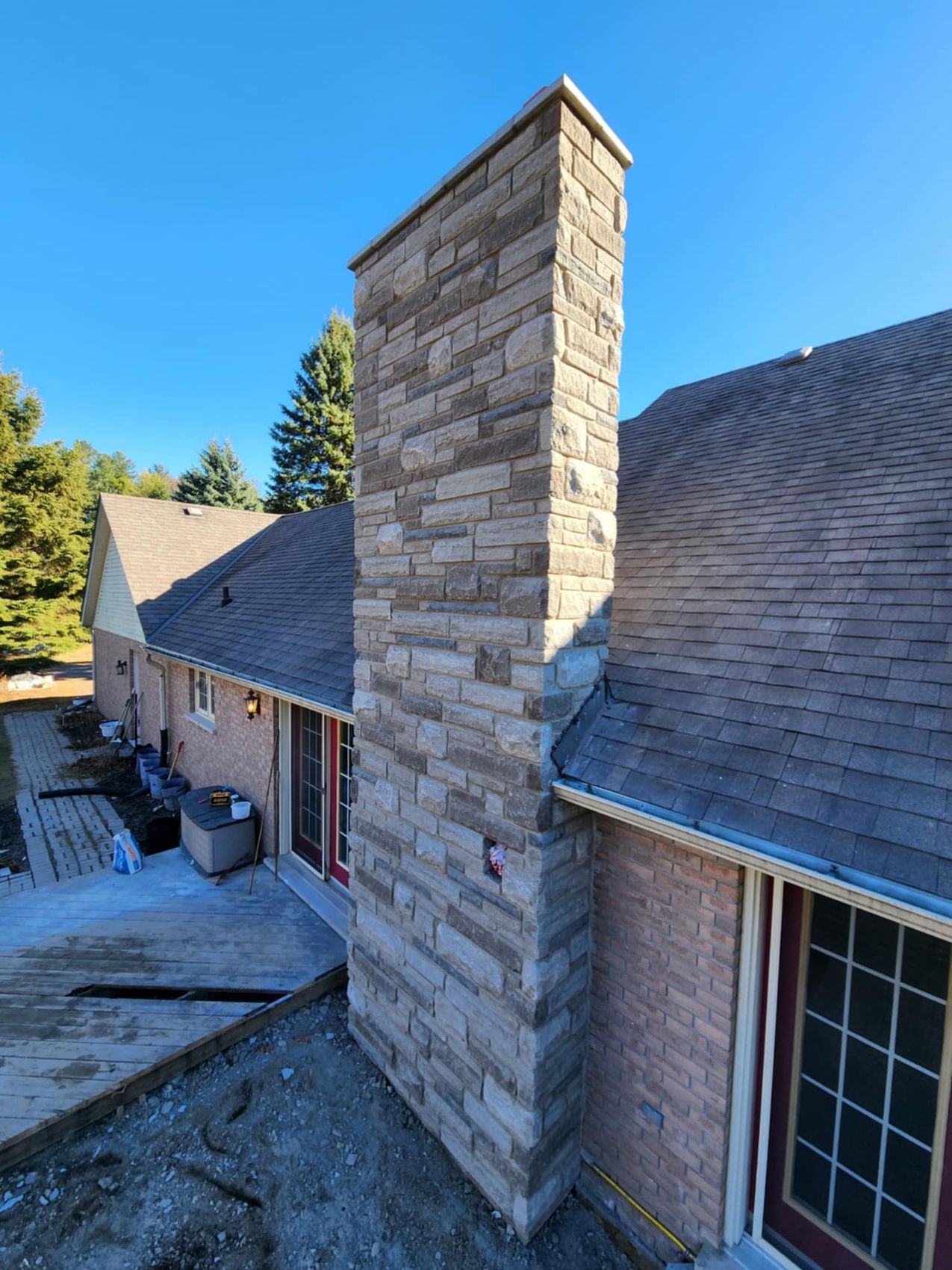 Tall stone-veneer chimney on a bungalow against a blue sky