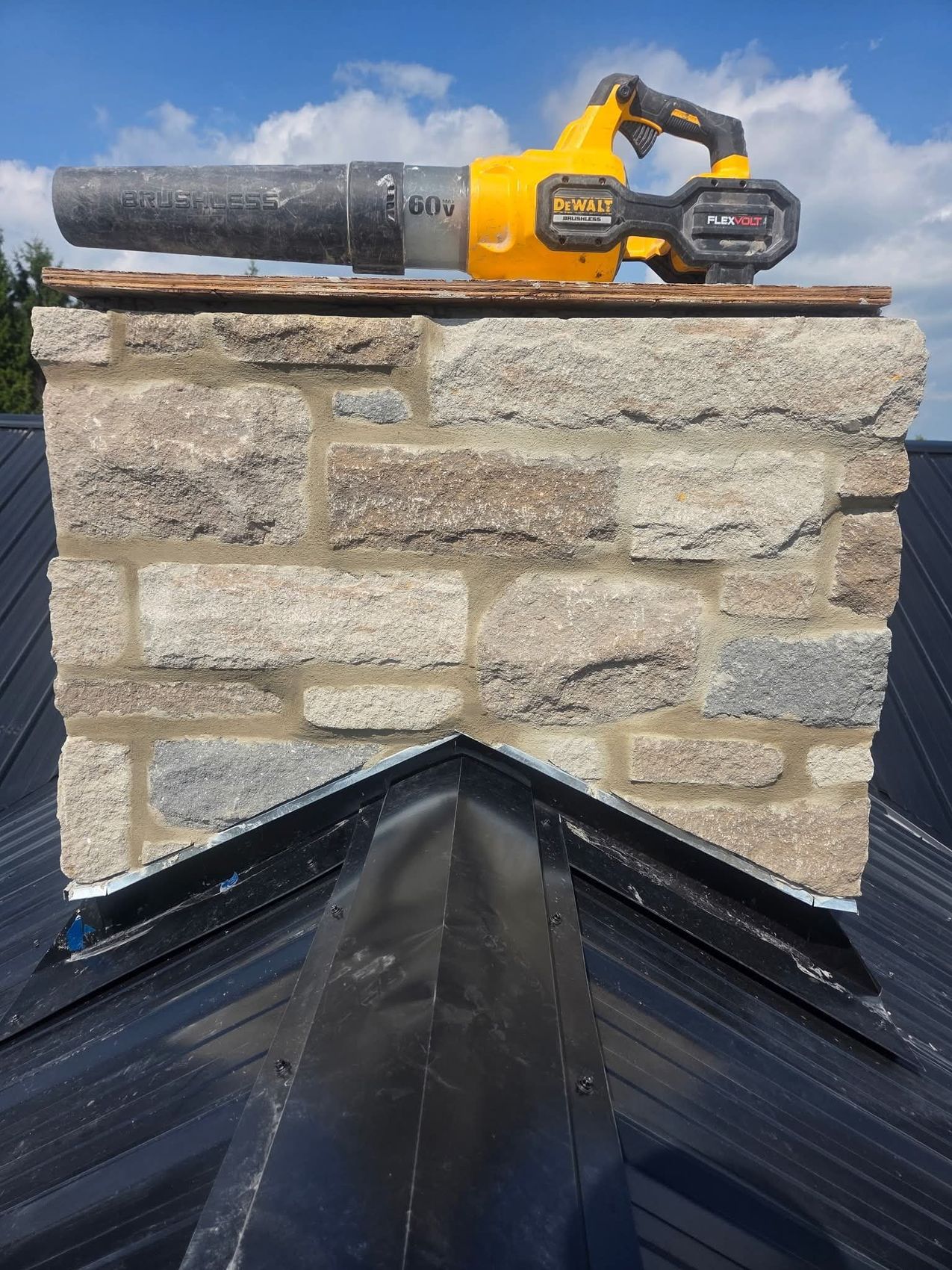Stone chimney top with new metal flashing on a black steel roof