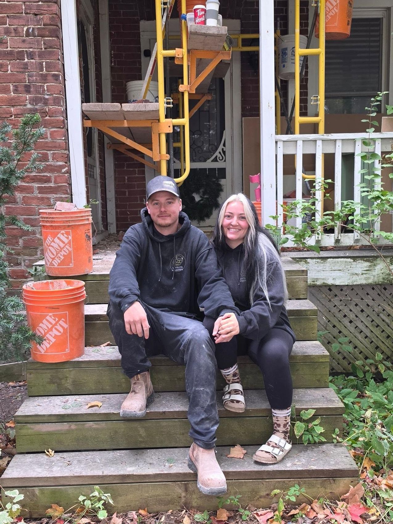Dallas Lyttle and Chantel Whyte sitting on the front steps at a job, scaffold behind them