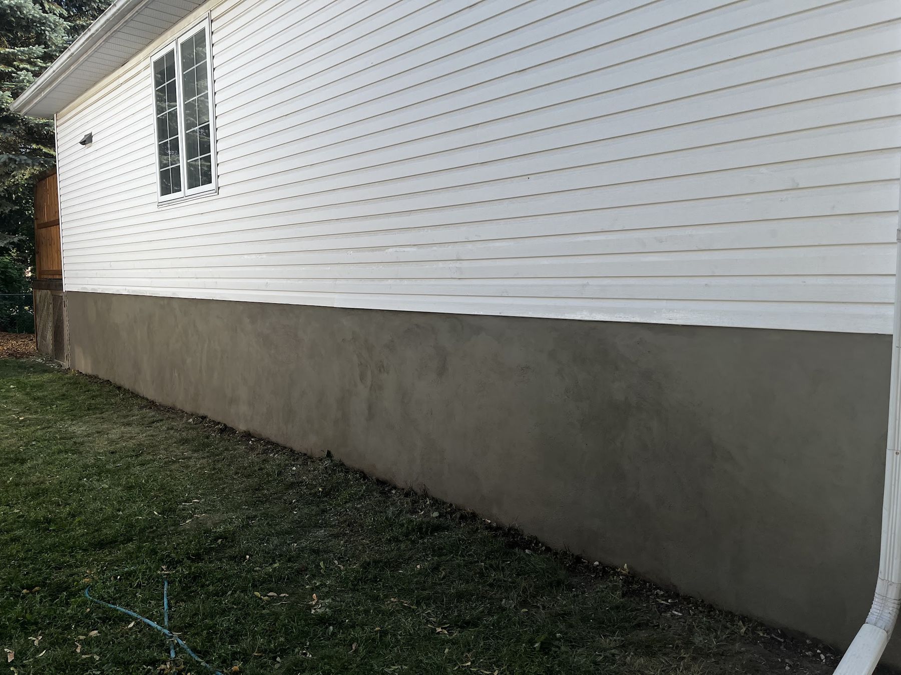 Freshly parged foundation below white siding