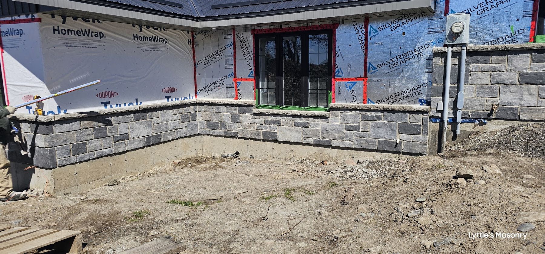 Stone skirt laid around the base of a new house wrapped in house wrap